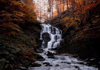 Beautiful waterfall with trees, red leaves, rocks and stones in autumn forest. Carpathian Mountains.