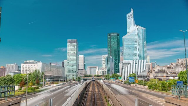 Office buildings in modern part of Paris - La Defense timelapse. Skyscrapers with rails of metro line and traffic on road. Paris, France