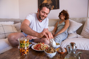 Couple eating healthy food from a delivery on the couch smiling