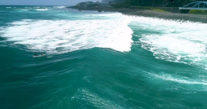 Aerial view of surf waves on the north coast of Madeira. Surfer on blue-green waves, drone shots. Cinema 4K, slow motion. Surfing in Madeira, Portugal.