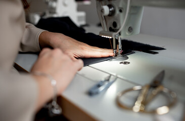 Close-up female hands sew a dark fabric on a sewing machine. Design studio, tailoring process concept.