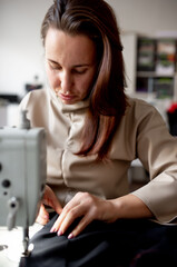 Fototapeta na wymiar A woman sews a dark fabric on a sewing machine. Design studio, tailoring process concept.