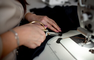 Obraz premium A woman sews a dark fabric on a sewing machine. Design studio, tailoring process concept.