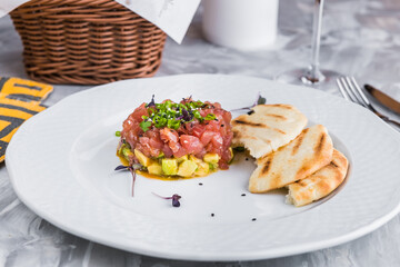 Salmon tartare with avocado on a white plate with tortillas