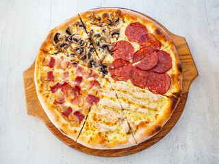 Round pizza with four different fillings cut into pieces on a wooden tray. Top view
