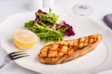 Grilled salmon steak with lemon and salad on a white plate