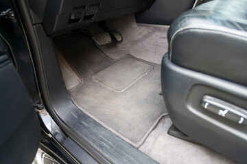 An open driver's seat door, a view of a dirty gray textile carpet stained under the control pedals before dry cleaning or washing. Car pre-sale preparation.