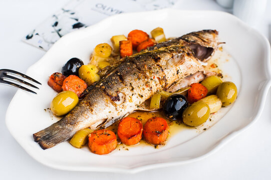 Grilled fish with garnish of carrots and olives on white plate