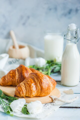 Croissants on a wooden board with a bottle of milk and white flowers on a light background