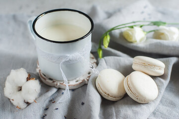 White macaroon cakes with a mug of milk on a gray napkin with white flowers