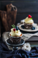 Capcakes with white cream, berries and a sprig of rosemary
