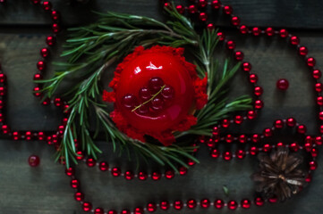 Red cake decorated with red currants on a dark background with a fir branch and red beads