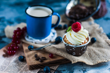 Capcakes with white cream, raspberry and mint with mug of milk