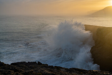 huge storm surge ocean waves crashing onto shore and cliffs at sunrise