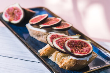 Bruschetta of baguette, cheese and figs are on a plate on the table. The concept of minimalism in food