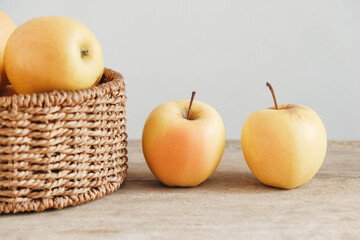 Yellow apples in a round wicker basket on a wooden table. Copy, empty space for text