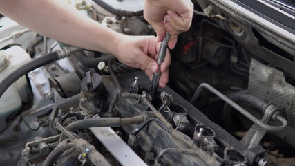 Fototapeta na wymiar A man pulls out an old spark plug from a car engine