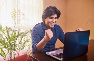 Hombre joven y feliz usando laptop o computadora en escritorio. Teletrabajo desde casa. Oficina en...