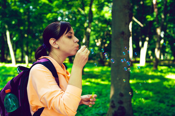 Young woman blowing bubbles on nature. Happy young brunette woman strolls in the Park and makes soap bubbles on a Sunny day