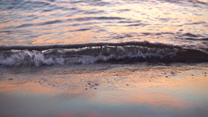 Evening relaxation on the beach. Beautiful waves at sunset, wet sand