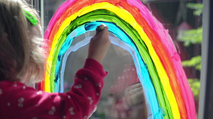 Fototapeta na wymiar Girl draws a rainbow with paints on the window
