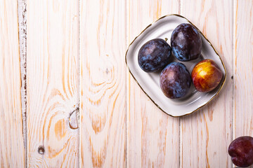 Fresh sweet plum fruits in white plate on wood table background, top view copy space