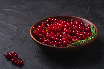 Fresh sweet red currant berries with rosemary leaves in wooden bowl, dark textured background, angle view