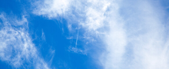 airplane in the blue sky with clouds from below, high flying passenger plane with condensation trail. jet plane flying overhead diagonally in sky with sunlight. Bottom view - Powered by Adobe