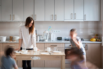 Children (blurred) having fun and running and tired mother in the messy kitchen