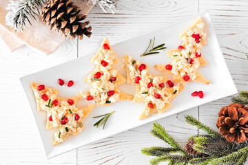 Christmas tree shaped appetizers with feta cheese, pomegranate and rosemary. Top view on a serving plate against white wood.