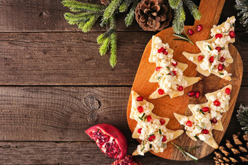 Christmas tree shaped appetizers with feta cheese and pomegranates. Top view on a serving board against a wood background. Copy space.