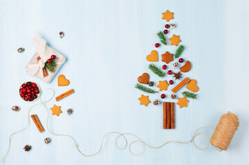 Christmas tree made of Xmas gingerbread cookies, cinnamons, cranberries and handmade furoshiki gift on blue background.
