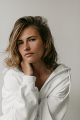 Fototapeta premium Portrait of beautiful young woman with brown hair and clean bronze skin without makeup on white background. Natural and healthy look. Neutral interior. Soft light. 