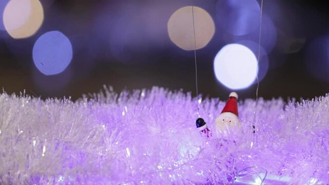 A toy Santa Claus slowly descends by parachute under the Christmas tree. Close-up