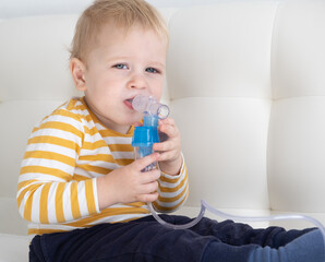 Little baby boy using steam inhaler nebulizer himself on the bed. copy space. health medical care.