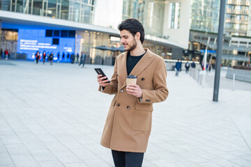 Man using his cellphone and holding a cup of coffee while walking in a city