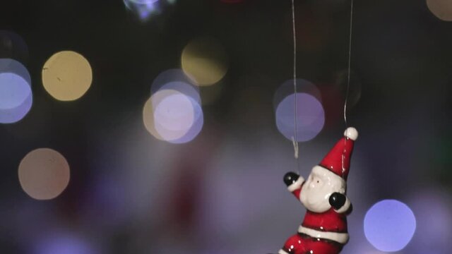 Toy Santa Claus flies on a parachute against the background of flickering multi-colored lights of the New Year's garland. Close-up