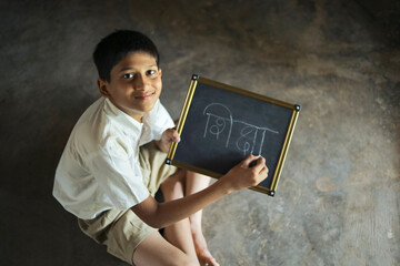 Cute indian child studying at home, writing shiksha word in marathi language on Slate board
