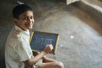 Cute indian child studying at home, writing shiksha word in marathi language on Slate board