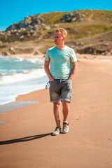 Handsome young blond man walks along the Black sea on the beach in sunny day