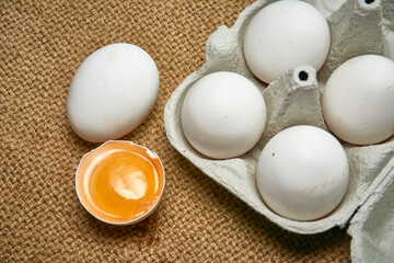 Fresh raw chicken eggs in a cardboard box on a burlap background.