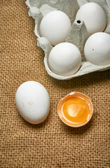 Fresh raw chicken eggs in a cardboard box on a burlap background.
