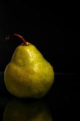 Close-up of fresh wet green pear on black background with reflection