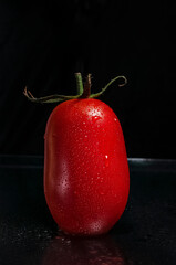 a red, fresh, ripe, juicy tomato with green leaves and drops of water on dark background with copy space for text