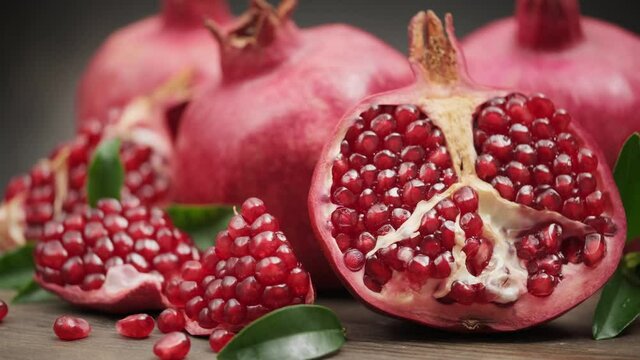 Pomegranate fruit and its half with leaves on a wooden board rotate on its axis on a dark background. 