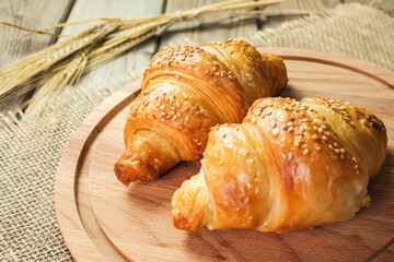 Freshly baked croissants on wooden cutting board, top view