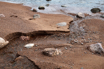 Sandy shore washed out by a stream. Blue sky reflected in smooth water. Autumn mood