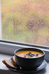 pumpkin and carrot cream soup with pumpkin seeds and toasted bread. on the windowsill, with cozy raindrops