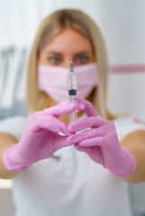 Doctor or nurse hand in pink gloves holding syringe with vaccine for a baby or adult. Medicine and drug concept.
