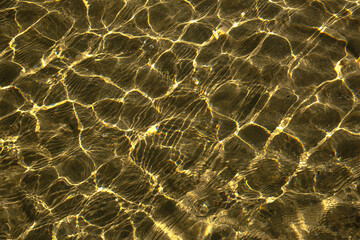 A whimsical pattern of glittering water on a sandy seabed. Shallow water on a sunny day. Morning sun. Close-up.